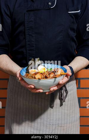 Ein professioneller Koch hält einen Teller Ramen Stockfoto