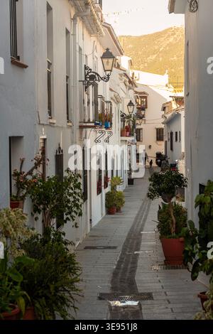 MIJAS, SPANIEN - 3. APRIL 2026: Enge Straße in Mijas Pueblo mit traditionellen weißen Fassaden, schmiedeeisernen Lampen und Blumentöpfen mit der Sierra d Stockfoto
