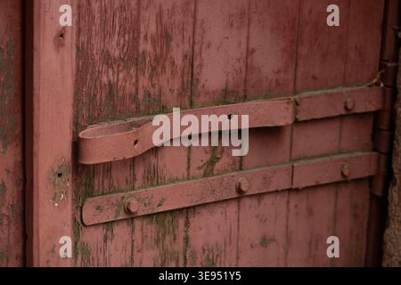 Rustikales rotes Holztor mit verwitterter Farbe und Vintage Metallscharnieren Stockfoto