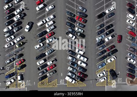 Blick aus der Vogelperspektive auf einen großen Parkplatz mit zahlreichen geparkten Autos, die in Reihen angeordnet sind. Stockfoto