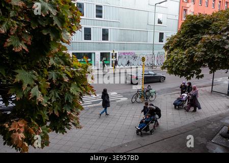 Die Leute laufen auf einem Bürgersteig in der Nähe eines Gebäudes mit Graffiti, während ein Auto auf der Straße fährt. Stockfoto