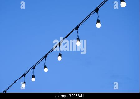 Reihe beleuchteter Glühbirnen, die an der Schnur und am blauen Himmel hängen Stockfoto