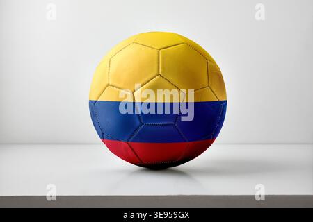 Ein Fußball mit den gelben, blauen und roten horizontalen Streifen Kolumbiens, der in der Mitte mit weichen Schatten auf einem neutralen Hintergrund platziert wird. Stockfoto