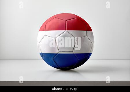 Ein Fußball mit den Farben der niederländischen Flagge in horizontalen roten, weißen und blauen Streifen, platziert auf einer weißen Oberfläche mit sanfter Beleuchtung. Stockfoto
