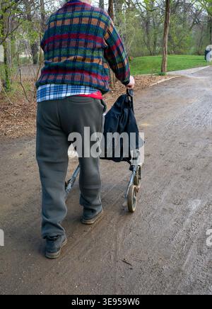 Ein alter Mann läuft mit einem Rollator im Regen durch den Park Stockfoto