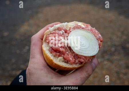 Ein halbes rohes, gehacktes Schweinefleisch mit Zwiebeln in der Hand Stockfoto