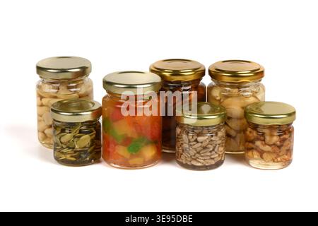 Studio-Aufnahme von sieben kleinen Glasgläsern mit goldenen Deckeln, die verschiedene konservierte Lebensmittel wie Cashewkerne, Erdnüsse, Sonnenblumenkerne, Kürbiskerne in Hone enthalten Stockfoto