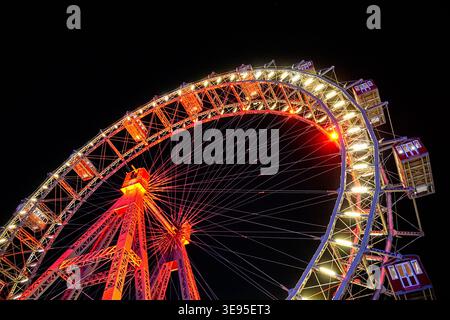 Riesenrad beleuchtet mit roten und weißen Lichtern, die sich nachts drehen, mit Gondeln, die vor dunklem Himmel im Vergnügungspark sichtbar sind Stockfoto
