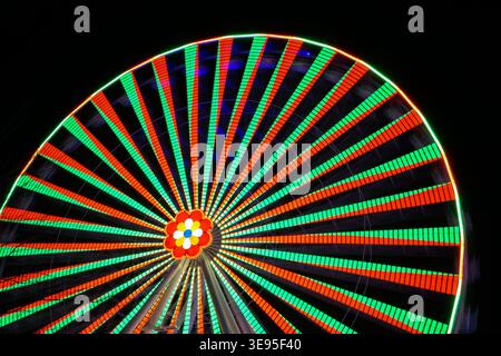 Das Riesenrad wird mit roten und grünen Lichtern beleuchtet, die sich bei längerer Belichtung nachts gegen dunklen Himmel drehen Stockfoto
