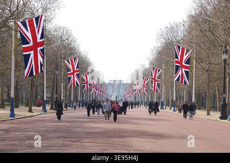 Touristen spazieren entlang der Mall, flankiert von Reihen von Union Jack Flaggen im St James's Park, die die Frühlings- und Sonnenscheinatmosphäre von London, Großbritannien, einfangen. Stockfoto