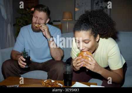 Multiethnische Paare essen Fast Food während der ungezwungenen Nacht in Stockfoto