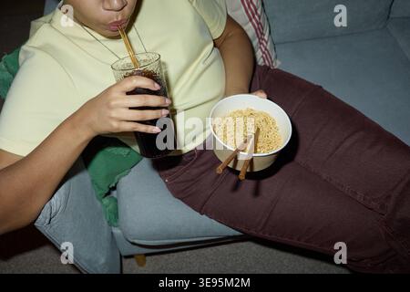 Erwachsene Frau trinkt Soda und isst Instant Nudeln zu Hause Stockfoto