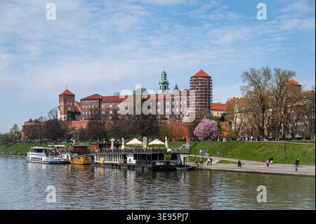 Krakau, Polen - 12. April 2026: Besucher spazieren an einem sonnigen Tag entlang des Flusses in der Nähe der Burg Wawel in Krakau, Polen Stockfoto