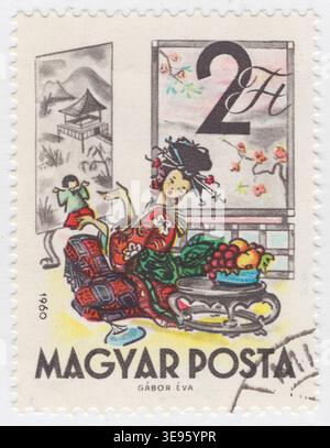 UNGARN - 1960. Dezember 1: 2 mehrfarbige Briefmarken zeigen eine Szene, die mit dem japanischen Volkshelden Momotaro, oder 'Peach Boy', verwandt ist. Eine Frau mit traditionellem Kimono und raffinierter Frisur sitzt auf dem Boden an einem niedrigen Tisch mit Früchten. Sie zeigt eine Geste auf eine kleine Figur des Helden. Im Hintergrund sind Shoji-Bildschirme mit einer Pagode, Bergen und Kirschblüten zu sehen. Das stilisierte Aquarellkunstwerk repräsentiert die kulturellen Wurzeln dieser Legende, in der ein älteres Ehepaar einen Jungen in einem riesigen Pfirsich durch eine europäische Linse aus der Mitte des Jahrhunderts findet Stockfoto