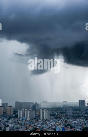 Dunkle Sturmwolken erheben sich über einer Stadtlandschaft. Regen strömt stark aus einer wirbelnden Trichterwolke. Gebäude stehen unter dem beklemmenden Himmel still. Urbane Szene Stockfoto