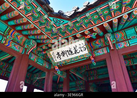 Aus nächster Nähe sehen Sie das komplizierte Dancheong (traditionelle dekorative Färbung) auf der Traufe eines koreanischen hölzernen Pavillons mit einer Kalligraphietafel mit Stockfoto