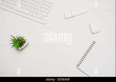 Minimaler Büroschreibtisch für Remote-Arbeiten mit weißer Tastatur, Anlage, Marker, Notebook und Ohrstöpsel auf Holz Stockfoto