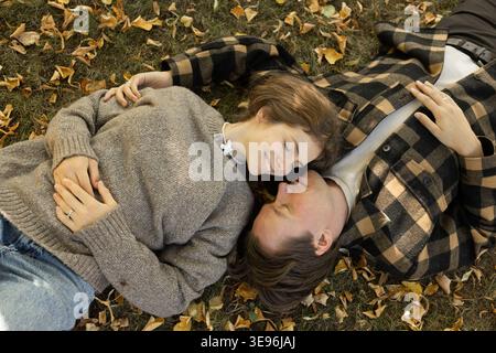 Niedliches junges Paar liegt auf den gefallenen Blättern, lächelt liebevoll und redet über ihre Gefühle. Stockfoto