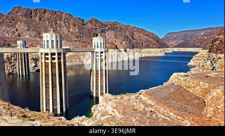 Der Hoover-Staudamm ist über dem Lake Mead. Malerische Aussicht auf die Einzugstürme des Hoover Dam, die sich vom Lake Mead erheben, mit Wüstenbergen, exponierter Küste und Stockfoto