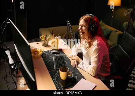 Kaukasische junge Erwachsene Frau streamt Live-Inhalte mit Headset und Mikrofon am Schreibtisch und erstellt Online-Medien. Nützlich für Bloggen, Influencer-Marketing, Remote-Work-Kampagnen Stockfoto