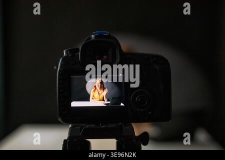 Nahaufnahme des Kamerabildschirms, der junge Erwachsene kaukasische Frau zeigt, die winkt, während sie am Schreibtisch Vlog-Stream aufzeichnet. Geeignet für Creator-Marketing, soziale Medien, Online-Kurse, Influencer-Branding Stockfoto