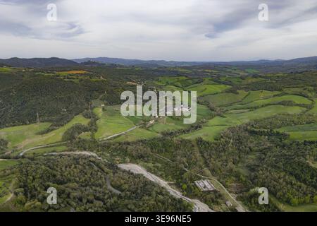 Aus der Vogelperspektive auf die üppig grünen sanften Hügel und dichten Wälder der toskanischen Landschaft mit einem kleinen Industriegebiet und einem trockenen Flussbett Pomarance, TUs Stockfoto