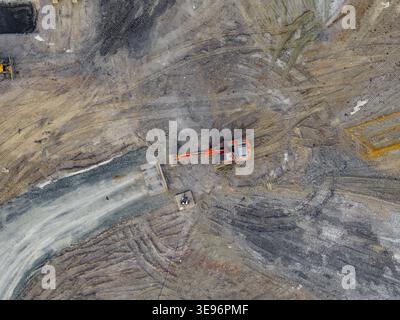 Luftaufnahme eines orangefarbenen Baggers, der auf einer Baustelle mit Reifenspuren auf dem staubigen Boden in Pomarance, Toskana, Italien arbeitet. Stockfoto