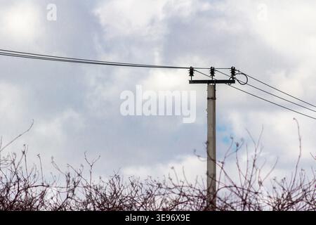 Stromleitungsposten mit Freileitungen gegen bewölkten Himmel, minimale industrielle Infrastruktur, Stromverteilung und Energieversorgungskonzept Stockfoto