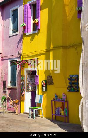 Farbenfrohe Burano-Häuser spiegeln sich entlang eines malerischen Kanals wider und schaffen eine lebendige und charmante venezianische Szene. Stockfoto