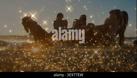 Fünf Frauen in Badeanzügen und Vertuschungen, die bei Sonnenuntergang am Sandstrand mit funkelndem Bokeh posieren Stockfoto