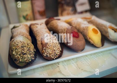 Verschiedene sizilianische Gebäckstücke auf weißem Teller. Cannoli mit Pistazien- und Schokoladenbelag, mit Marmelade gefülltes Gebäck mit farbenfrohen Dekorationen. Verz Stockfoto
