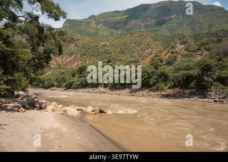 Der Chicamocha River fließt durch eine Canyonlandschaft mit einem sandigen Flussufer, felsigen Ufern und dichter grüner Vegetation, die die umliegende steile mou bedeckt Stockfoto