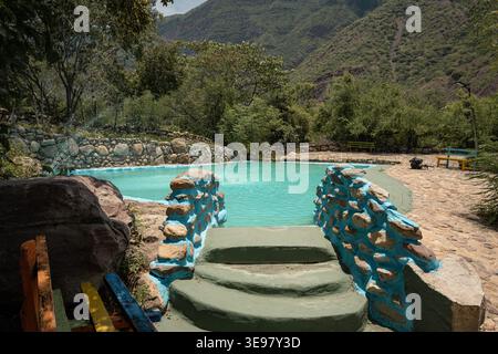 Der Pool des Resorts mit rustikalen Felswänden, grünen Stufen und türkisfarbenem Wasser bietet einen erfrischenden Rückzugsort inmitten üppiger Bäume und einer malerischen Landschaft Stockfoto
