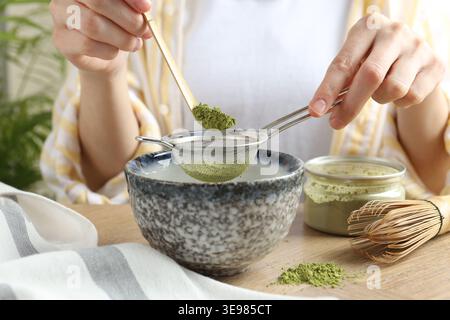 Frau, die Matcha-Pulver in eine Schüssel am Holztisch siebt, Nahaufnahme Stockfoto