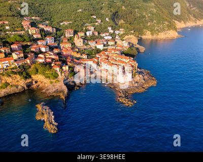 Blick aus der Vogelperspektive auf das farbenfrohe Küstendorf Tellaro, das auf felsigen Klippen mit historischen Häusern und üppigen grünen Hügeln mit Blick auf das blaue Mediterr thront Stockfoto