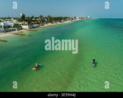 Aus der Vogelperspektive auf Paddleboards im türkisfarbenen Wasser entlang eines Sandstrandes mit Palmen und Häusern an der Küste in Yucatan, Mexiko. Stockfoto