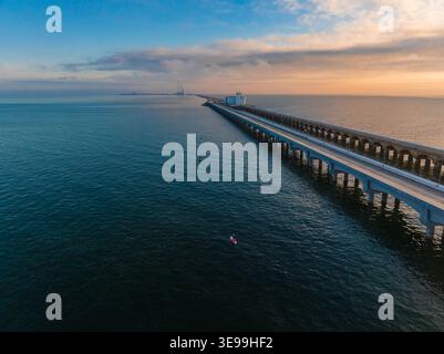 Aus der Vogelperspektive auf den Long Progreso Pier, der sich über den ruhigen blauen Ozean erstreckt, mit Menschen auf Paddleboards unter einem weichen Sonnenuntergangshimmel in Yucatan, Mexiko. Stockfoto