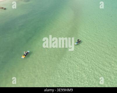 Aus der Vogelperspektive sehen zwei Personen auf Paddleboards, die über klares türkisfarbenes Wasser über einen sandigen Meeresboden Yucatan, Mexiko, gleiten. Stockfoto