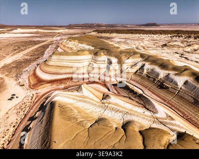 Aus der Vogelperspektive der farbenfrohen, geschichteten Felsformationen der Kyzylkum-Wüste unter einem klaren blauen Himmel in Kyzylkum, Region Mangystau, Kasachstan. Stockfoto