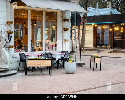 Jurmala, Lettland - 29. März 2026: Sitzbereich im Freien außerhalb der Saison mit Tischen, die mit Blumen geschmückt sind, vor einem lokalen Restaurant, das eine Dekora zeigt Stockfoto