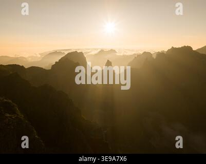 Aus der Vogelperspektive auf Pico do Arieiro mit zerklüfteten Berggipfeln und Sonnenstrahlen, die durch den Morgennebel in Curral das Freiras, Madeira, Portugal, dringen Stockfoto