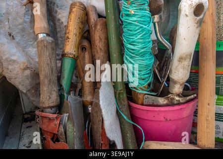 Handwerkzeuge für Gartenarbeit, die auf dem Boden in einer Ecke eines Gewächshauses gelagert werden Stockfoto