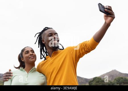 Ein Paar lächelt beim Selfie in den Vorbergen, ein Mann hält ein Smartphone, beide tragen Activewear Stockfoto