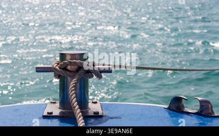 Pollerbefestigung auf dem Bootsdeck in Thailand. Das Seil ist sicher am Metallpfoller befestigt. Glitzerndes blaues Meer im Hintergrund. Stockfoto