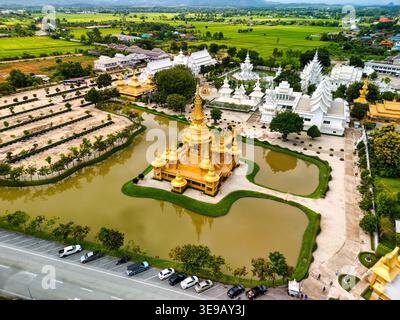 Blick aus der Vogelperspektive auf das kunstvoll verzierte goldene Gebäude am Wat Rong Khun, umgeben von einem reflektierenden Teich und üppigen grünen Feldern in Pa O Don Chai, Chiang Rai, Thailan Stockfoto