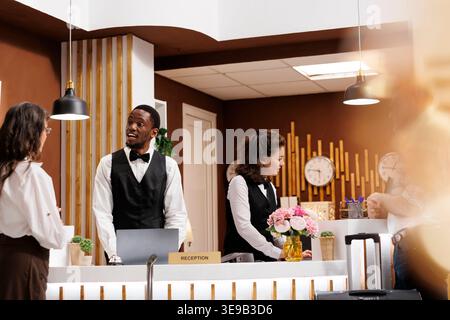 afroamerikanischer männlicher Rezeptionist hilft pensionierten Seniorinnen beim Check-in in der Hotellobby. Professionelle Mitarbeiter bieten außergewöhnlichen Kundenservice für ältere Touristen. Stockfoto