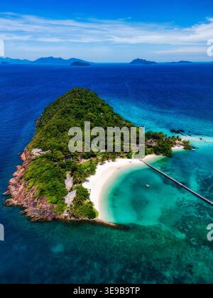 Blick aus der Vogelperspektive auf die Insel Ko Kham mit weißem Sandstrand, türkisfarbenem Wasser und einem langen Holzpier, umgeben von üppigem tropischem Wald in Ko Mak, Tra Stockfoto