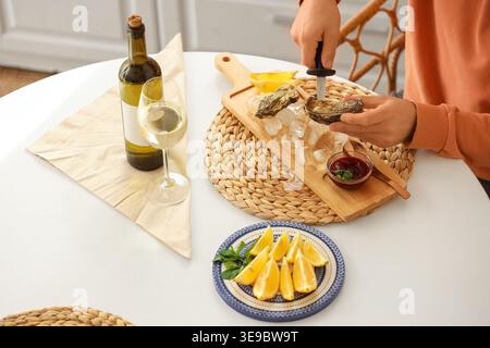 Junger Mann, der zu Hause frische Austern mit Messer öffnet Stockfoto