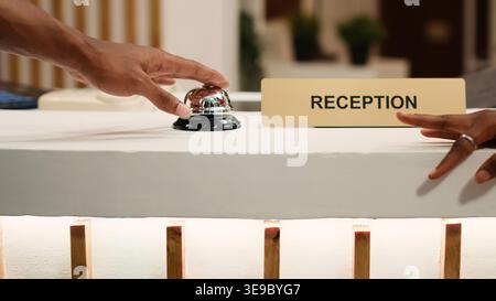 Nahaufnahme von afroamerikanischen Gästen, die an der Rezeption die Serviceklingel läuten und ihre Zimmerreservierung buchen können. Concierge-Mitarbeiter geben beim Einchecken von Touristen Daten ein Stockfoto