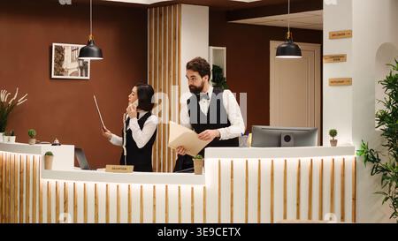 Professionelle Teamwork-Mitarbeiter an der Rezeption überprüfen die Urlaubspakete für Gäste an der Rezeption. Das Hotelpersonal buchte eingehende Touristen und arbeitete in der stilvollen Resort-Lounge Stockfoto